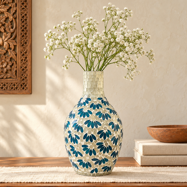 A glass mosaic vase with a blue and white floral pattern, filled with white baby's breath flowers, displayed on a wooden table in a styled interior setting.